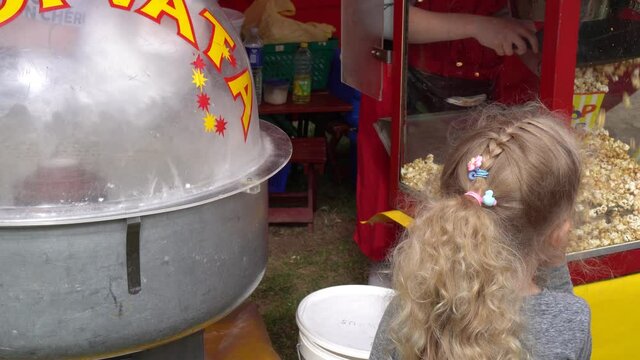 Caucasian girl standing between candyfloss and popcorn machines. Child choosing sweets. Gimbal stabilizer motion movement shot.