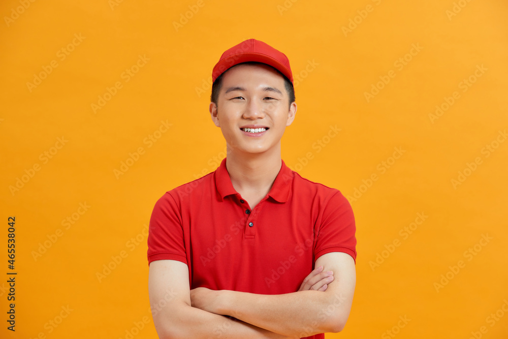 Poster smiling delivery man in red uniform standing with arm crossed - isolated on white background