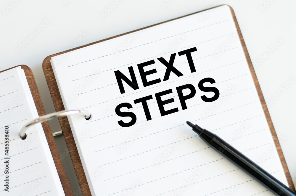 Aufkleber next steps text on notepad on table next to black marker business concept