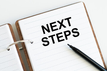 Next Steps text on notepad on table next to black marker business concept