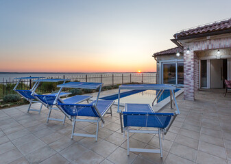 Terrace with swimming pool and deck chairs at sunset