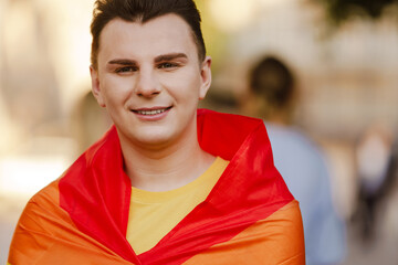 White man smiling and holding rainbow flag during pride parade at city