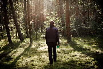 Man holding green coffee cup while walking in forest during sunny day.