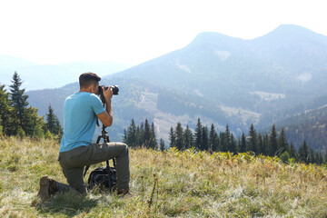Fototapeta na wymiar Man taking photo of mountain landscape with modern camera on tripod outdoors