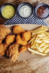 Top view of chicken nuggets, batter wings and fries. A set of three dishes in a paper box. Fast food cafes and restaurants. The food is laid out in a row. Three types of sauce
