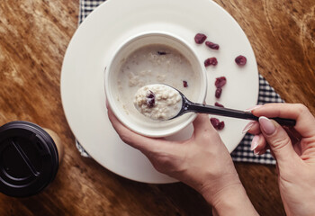 Close-up of oatmeal in a paper cup. Takeaway food. Healthy breakfast with raisins, dried apricots and milk. Wooden background. Nearby is coffee to go