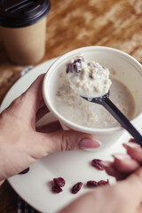 Close-up of oatmeal in a paper cup. Takeaway food. Healthy breakfast with raisins, dried apricots and milk. Wooden background. Nearby is coffee to go