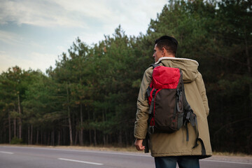 Man with backpack on road near forest, back view