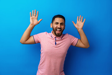 Fototapeta premium Portrait of amazed brunette man with beard in pink t-shirt against blue background