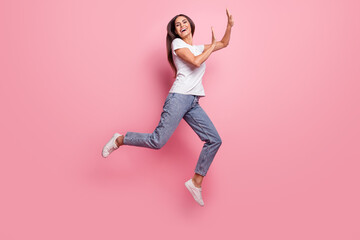 Fototapeta na wymiar Full size profile photo of impressed young brunette lady jump wear t-shirt jeans sneakers isolated on pink background
