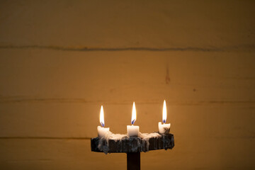 Three lit candles in a candle holder with wax melting from it on an old wall