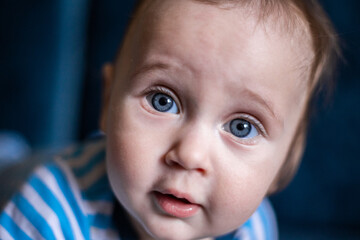 A kid with big blue eyes looks at the camera in surprise, a close-up of his face. High quality photo