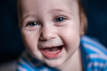 A smiling toothless kid in a striped blouse laughs, face close-up. . High quality photo