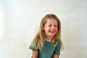 portrait of a happy child on a white background in a green t-shirt smiling. The little girl plays with her sly eyes. Happy girl. copy space. Childhood concept.