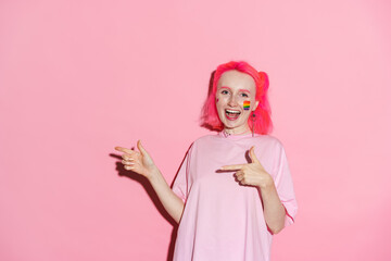 Young woman with rainbow makeup smiling while pointing fingers aside