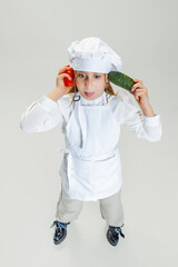 High angle view of little cute girl in white cook uniform and huge chef's hat posing isolated on white studio background.