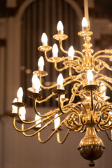 A gold plated chandelier with lights in front of a prospect of a pipe organ