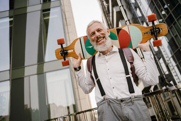Grey mature man standing with skateboard at city street