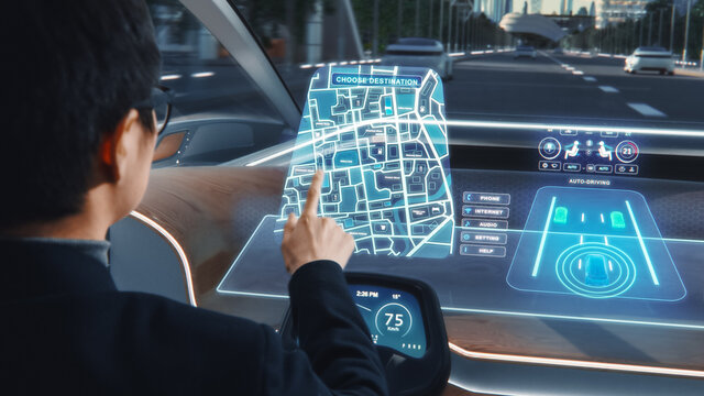 Futuristic Concept: Stylish Businessman Setting Location on an Interactive Navigation App on an Augmented Reality Dashboard while Sitting in an Autonomous Self-Driving Zero-Emissions Electric Car. 