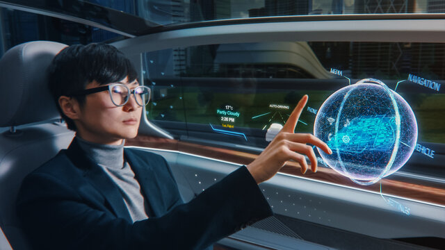Futuristic Concept: Stylish Businessman Setting Location on an Interactive 3D Navigation App on an Augmented Reality Dashboard while Sitting in an Autonomous Self-Driving Zero-Emissions Electric Car. 