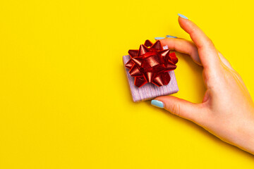 Hand with a gift box on yellow background with free space for text, list of presents for boxing day on Christmas eve.