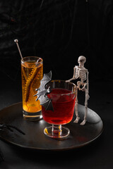 Halloween red and orange alcoholic cocktails decorated bat and skeleton on black background. Horror funny beverage for festive party.