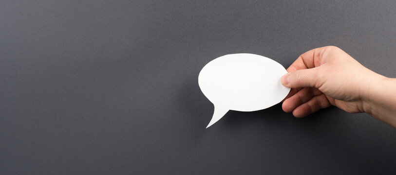 Hand holding a white speech bubble, grey colored background, copy space, message, communication - Powered by Adobe