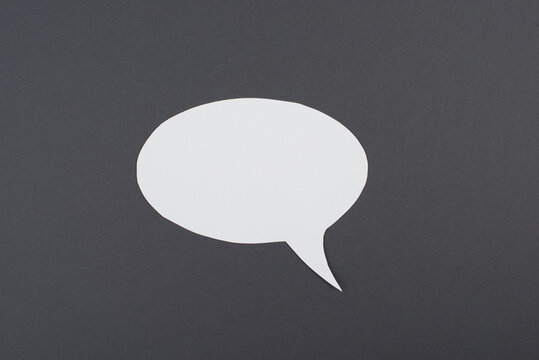 Empty speech bubble, white paper on a dark grey background, copy space for text, communication symbol