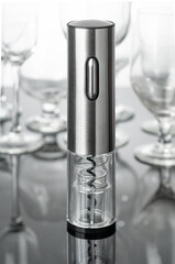 Electric corkscrew in gray metal. Stands on a mirrored surface. Empty glass goblets in the...