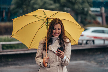Woman using smartphone and holding a yellow umbrella during a heavy rain in the city
