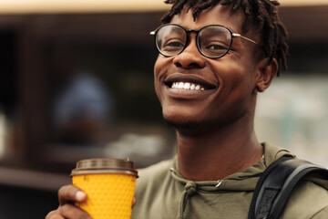 Image of smiling hispanic man, walking down city street holding takeaway coffee