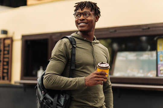 African American male student, wearing glasses, drinking coffee on the street in the city