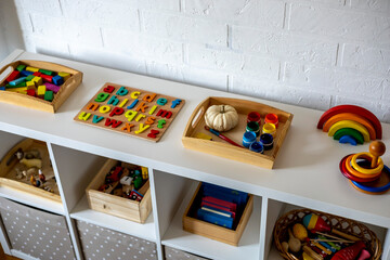 White shelf with baskets and drawers in the children room. Montessori material. Home schooling concept.