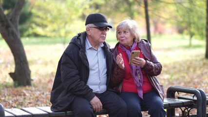 Happy senior couple laughing and exciting with something in smartphone mobile while sitting in the park