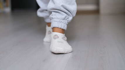 Legs of a woman in white socks walking on the wooden floor of her house with a sofa in the background. feet wearing white socks on gray wooden floor