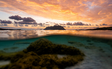 (Selective focus) Split shot, over under water surface. Defocused waves in the foreground with Tavolara Island on the surface during a dramatic sunrise. Porto Istana, Sardinia, Italy.