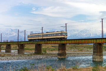 北アルプスを背景に、常願寺川橋梁を渡る富山地方鉄道本線の電車