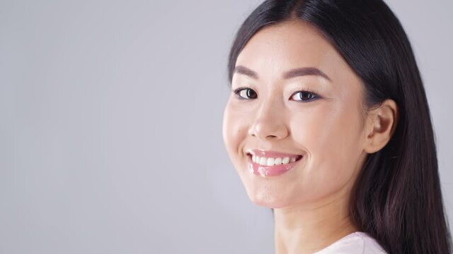 Side view portrait of young asian lady with perfect hair turning to camera and smiling, empty space, slow motion