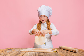 Portrait of little beautiful girl in white cook uniform and huge chef's hat at kids kitchen...