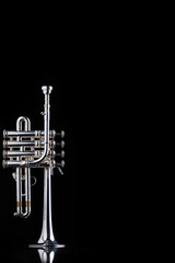 A four valve piston silver plated piccolo trumpet on a black reflective surface. A brass instrument common to baroque music.