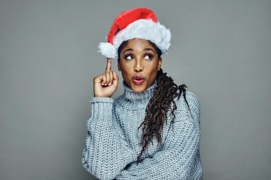 Thoughtful attractive young woman wearing Santa hat and sweater against gray background