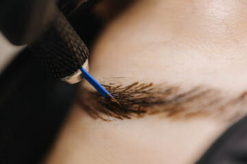 eyebrow microblading. A master in black gloves holds a blending needle over the brow of the model....
