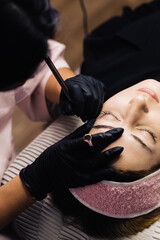 eyebrow microblading. A master in a transparent mask on his face and black gloves holds a handpiece...