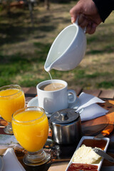 sirviendo leche en una taza, desayuno para dos personas al aire libre sobre una mesa de madera,...