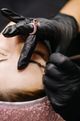 Fototapeta na wymiar eyebrow microblading. A master in black gloves holds a blending needle over the brow of the model. Macro photography