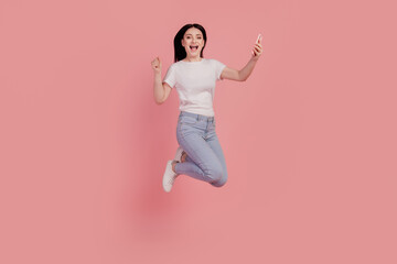 Photo of online casino bet player lady jump hold phone win dream crazy prize isolated on pink color background