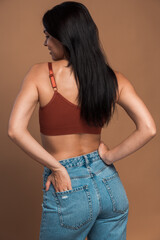 Back view of the alluring brunette woman in top and jeans looking away while posing to the camera...
