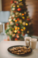 Christmas background with homemade gingerbread and two cups of hot cocoa, christmas lights on the Christmas tree, bokeh