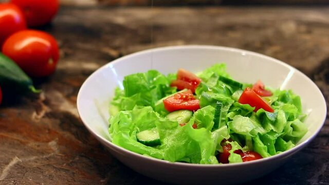 housewife pours olive oil on fresh vegetable salad with lettuce leaves on a plate. Cooking a delicious salad of tomatoes, cucumber with salad in the kitchen at home. Healthy tasty food at home