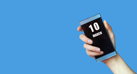 march 10. 10th day of the month, calendar date.Woman's hand holds mobile phone with blank screen on blue isolated background.Spring month, day of the year concept